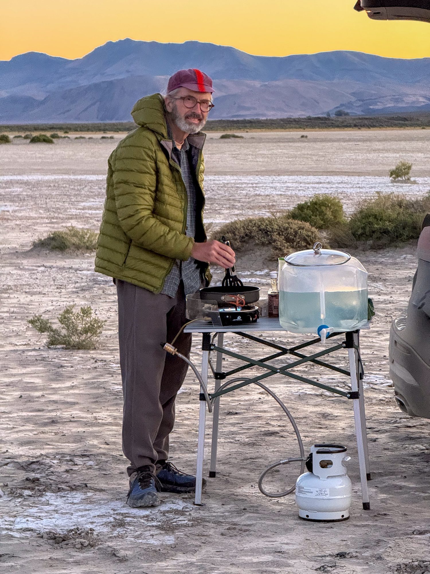 James cooking dinner at camp, Steens Mountain glowing behind at sunset