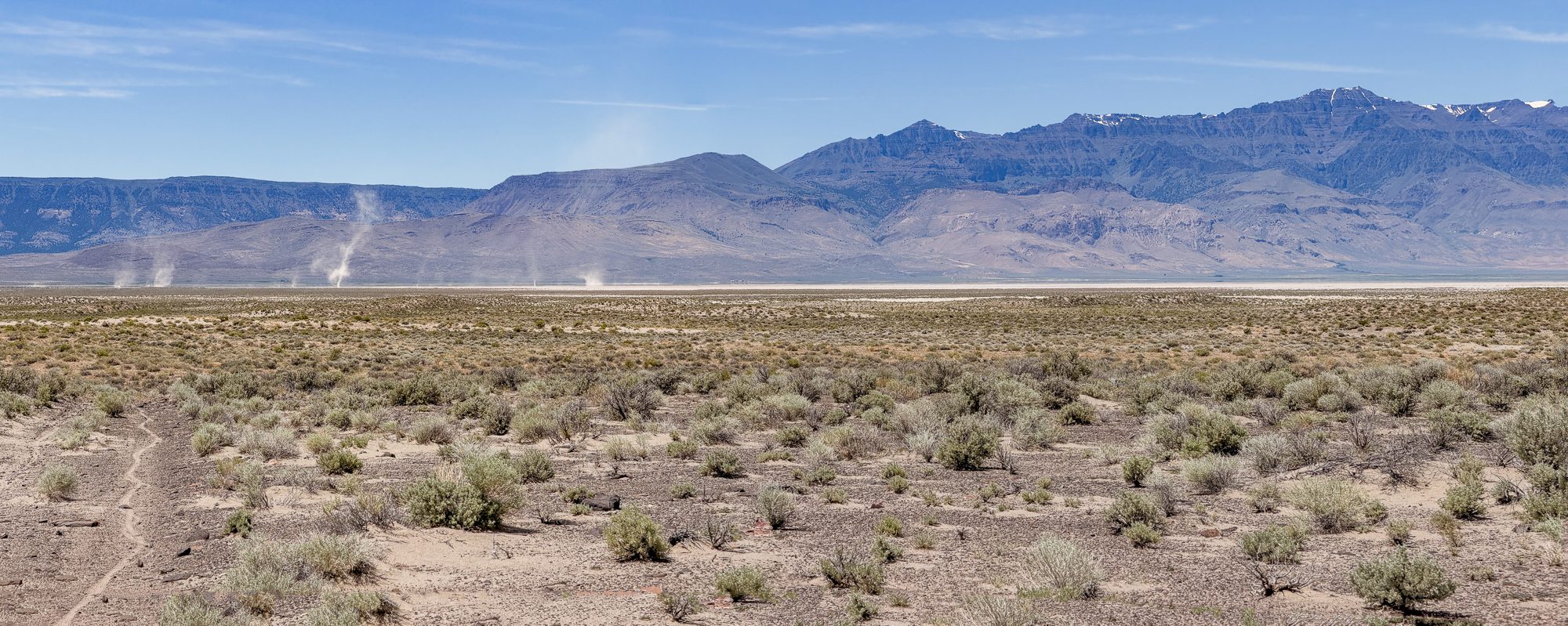 Panorama from high ground showing three dust devils rising from the Alvord Playa with Steens Mountain beyond