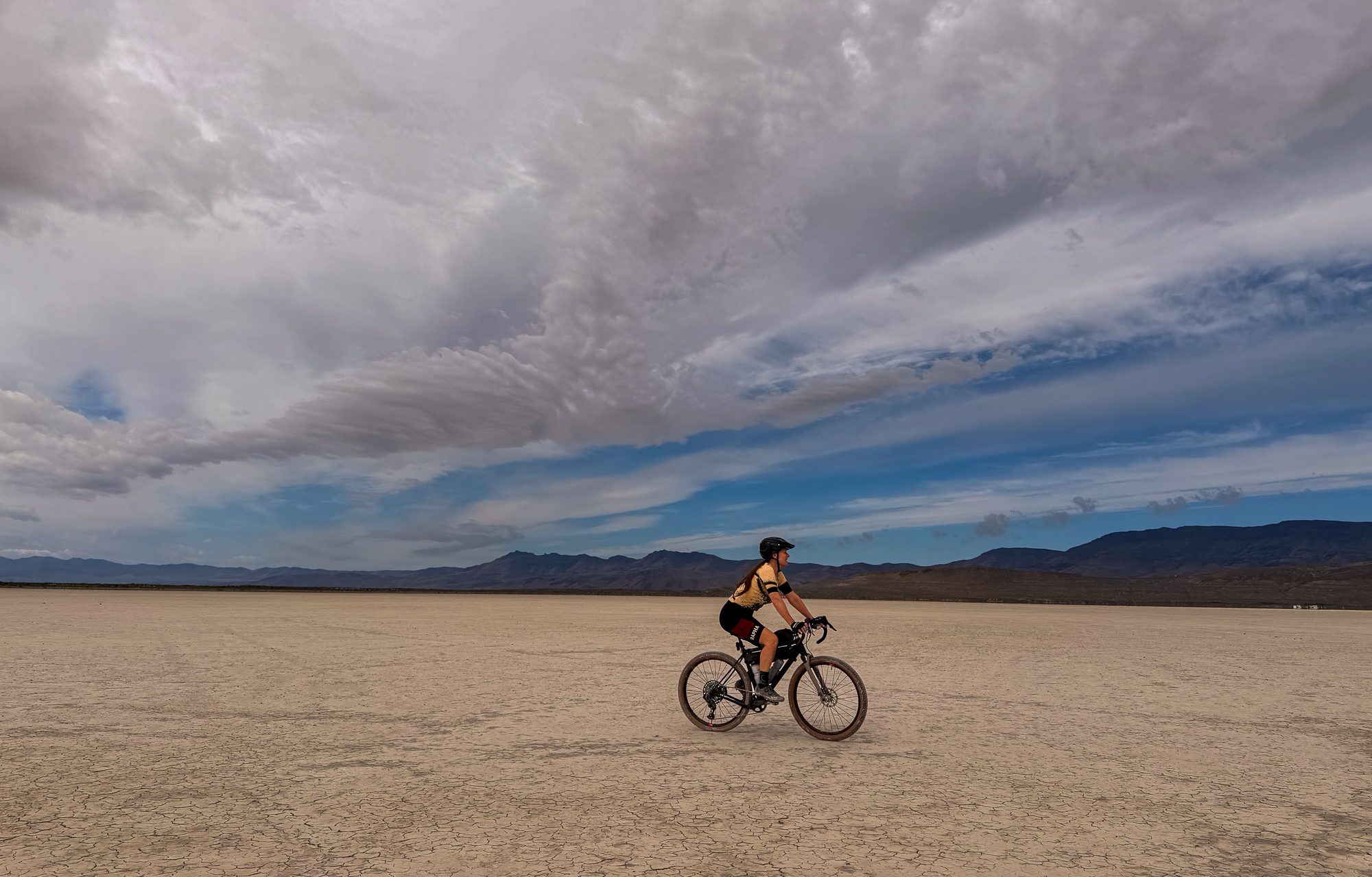 Amy riding on the open playa under a dramatic sky of towering cumulus clouds