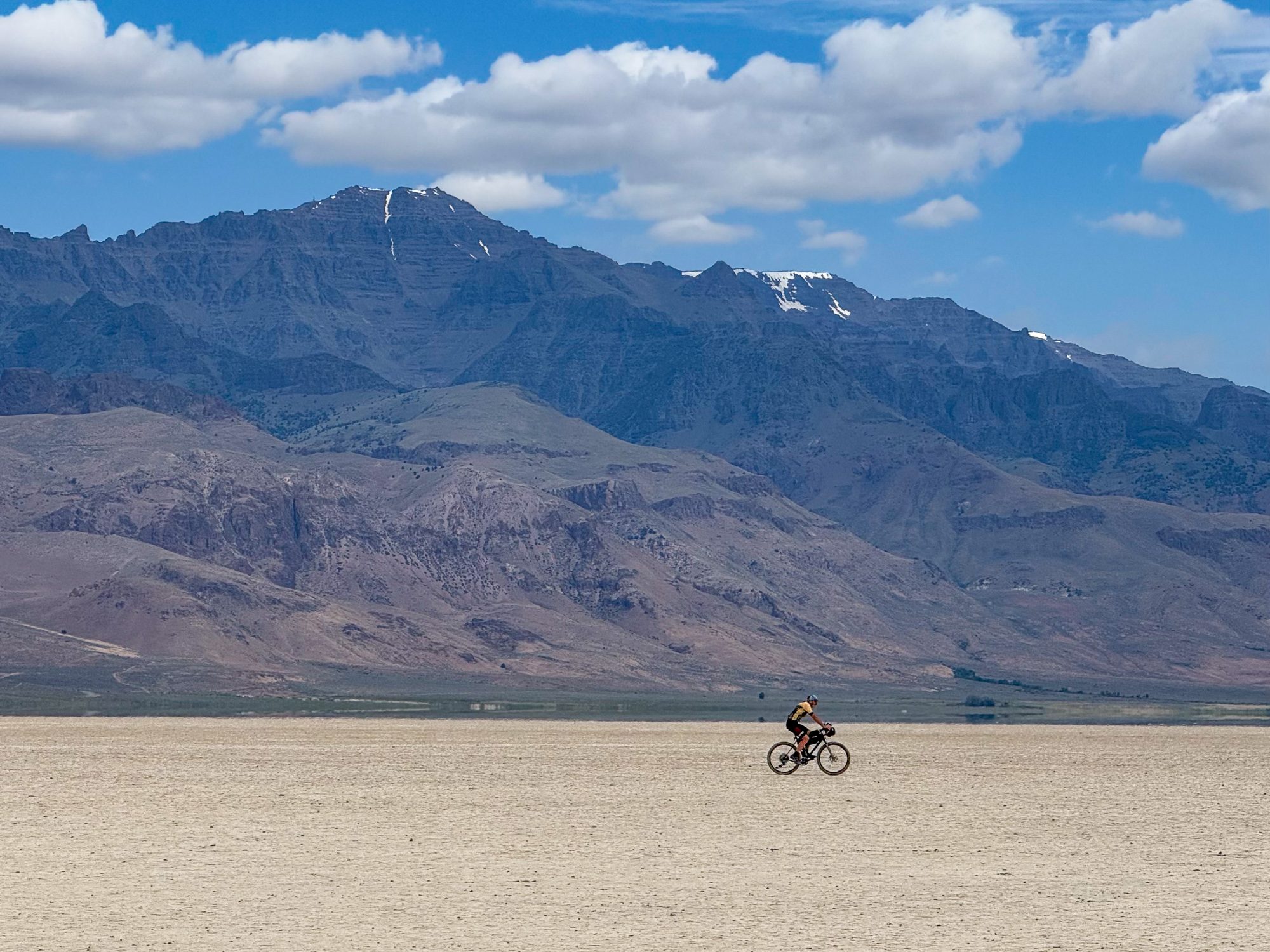 Single rider tiny on the vast Alvord Playa, Steens Mountain rising dramatically behind