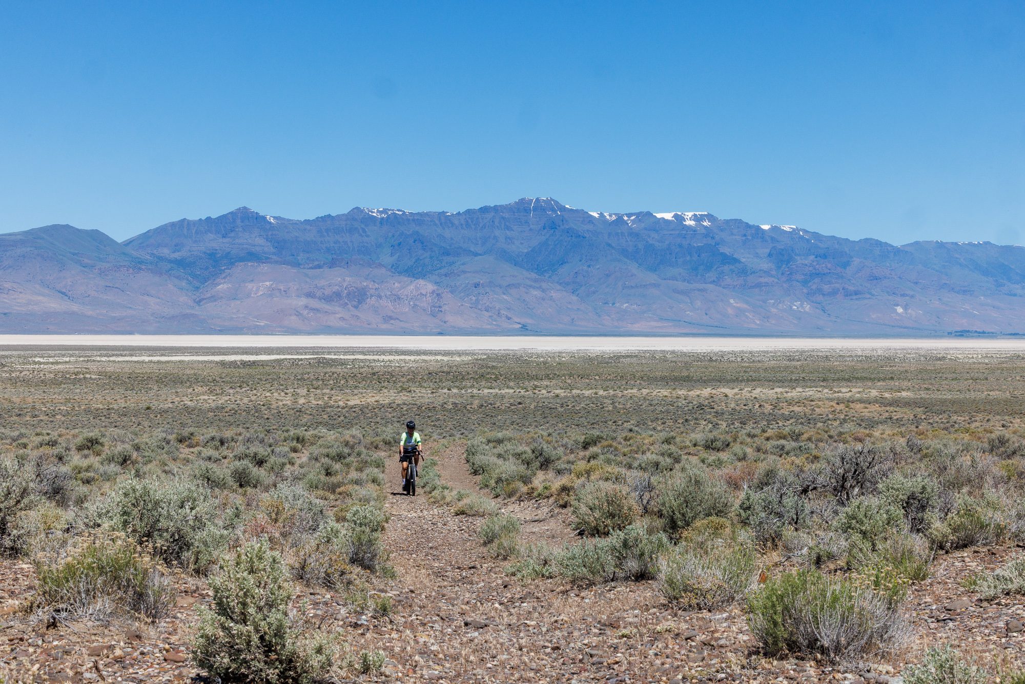 Tiny rider alone in vast sagebrush landscape, Alvord Playa visible in distance