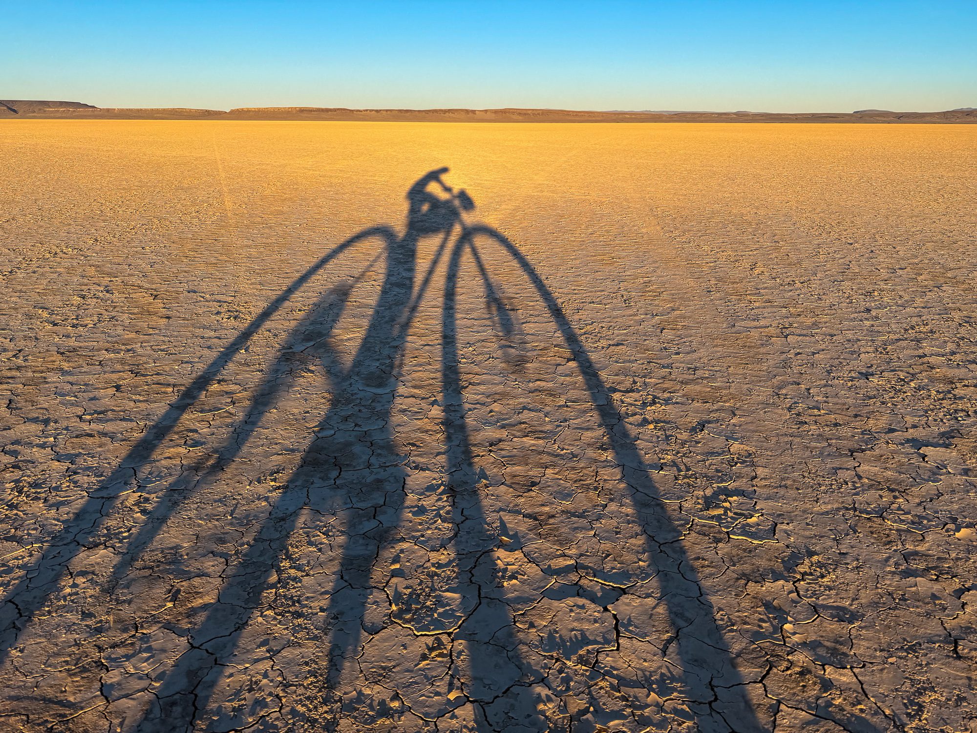 Long afternoon shadows of cyclist and bicycle on the cracked Alvord Playa