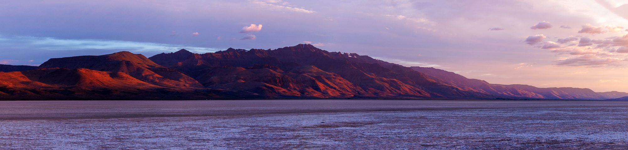 Panorama of Steens Mountain glowing deep red and purple at sunrise over the Alvord Playa