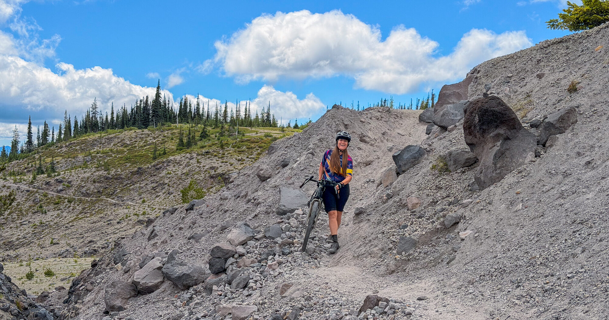 A rider descending a steep wash of grey pumice under a blue sky